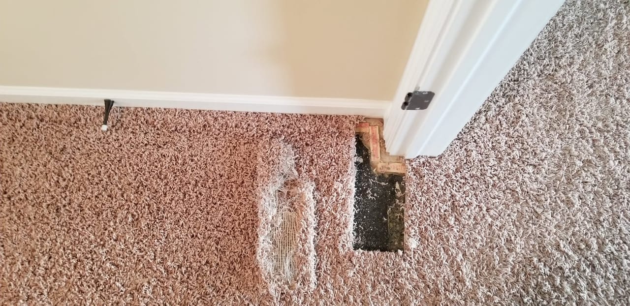 Carpet repair in progress beside a door frame: the damaged section cut out, with the worn piece lying next to the opening