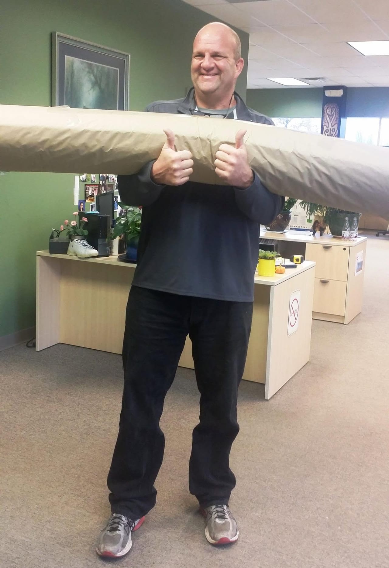 A smiling customer giving two thumbs up while carrying his rolled rug on his shoulder in the Langenwalter shop
