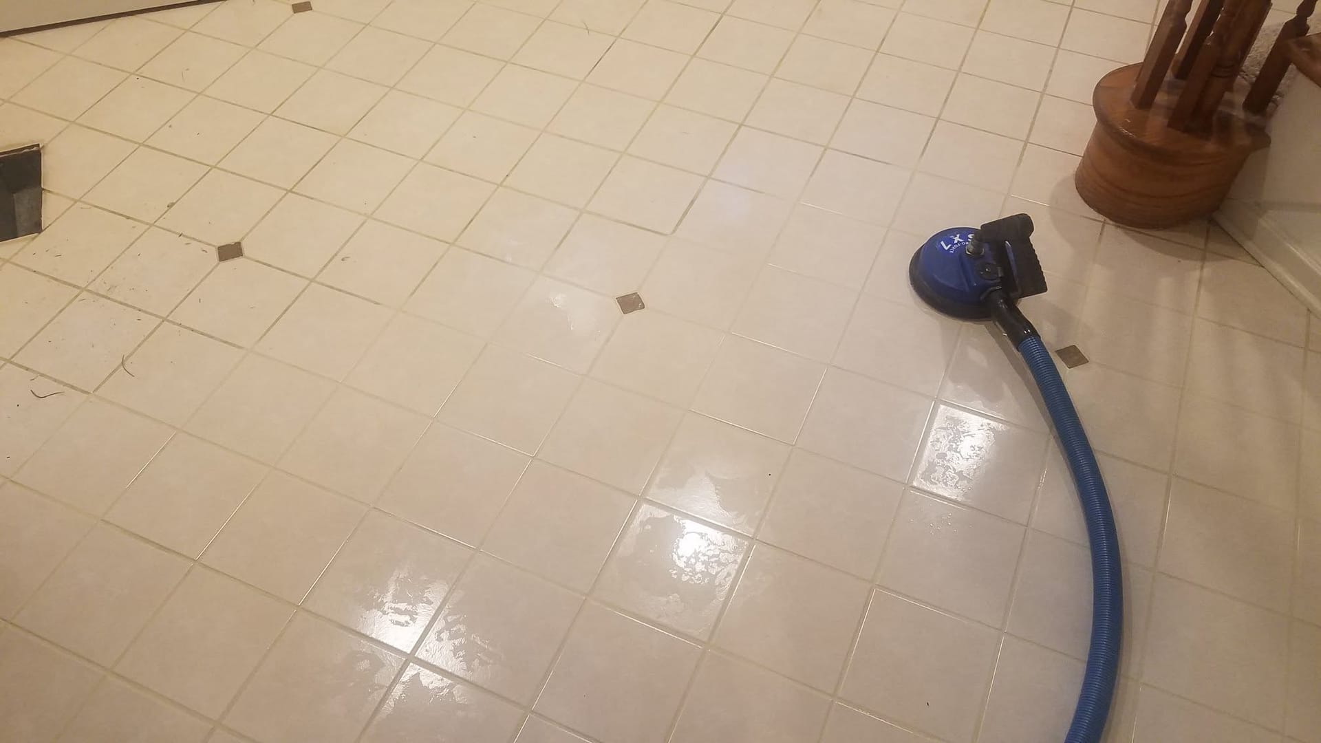 A tile and grout cleaning tool on a white tile floor halfway through cleaning