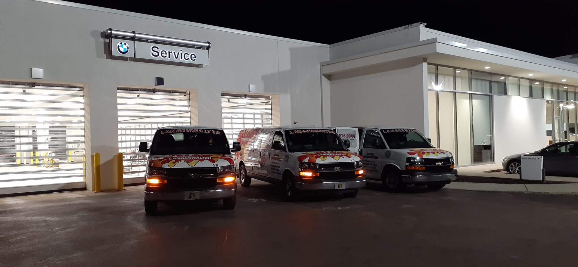 Three Langenwalter vans parked outside a car dealership service center at night